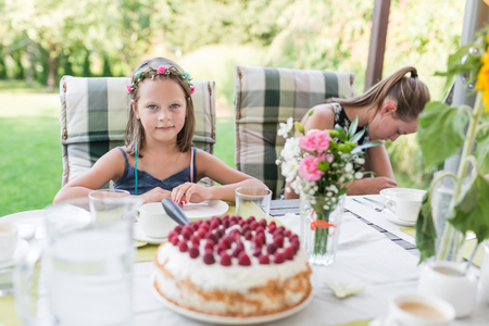 little laughing girl at her birthday party on the garden terrace sitting at the table with a birthday cake - authentic family lifeの写真素材