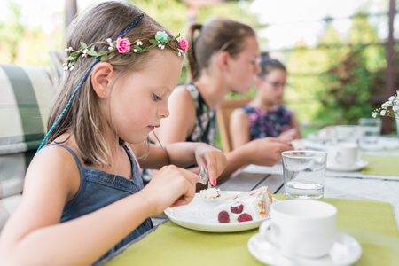 little laughing girl at her birthday party on the garden terrace sitting at the table with a birthday cake - authentic family lifeの写真素材