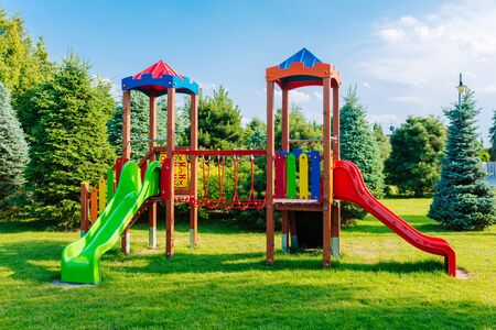 Colorful empty playground in summer scenery with green trees in the background