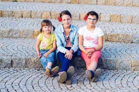 Three sisters sitting on stone stairs - during summer holidays