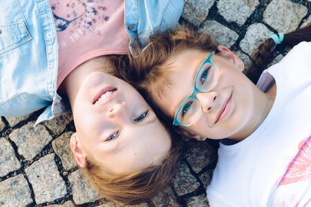 Two young blonde girls lying on the ground with eyes open and their heads side by side. View from...