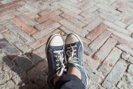 Foot and legs seen from above on a brick, rustic background. Selfie of sneakers on the floor great for any use.の写真素材
