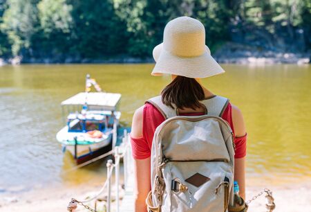 Girl in a straw hat and backpack on the banks of the river in anticipation of a cruise on a tourist boatの写真素材