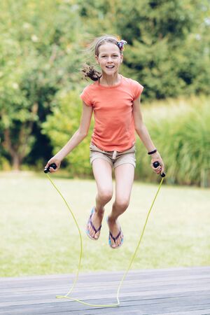 Laughing teenage girl jumping rope in the garden on the terrace in summerの写真素材