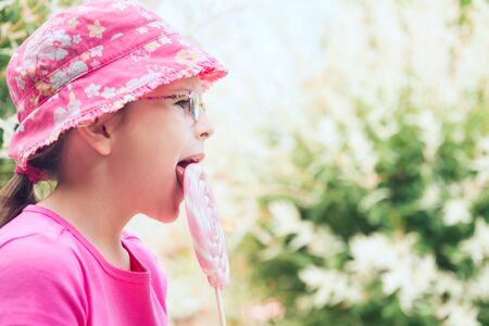Little girl in a pink hat licking big lollipopの写真素材