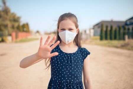 Coronavirus and air pollution concept. Little Caucasian girl wearing face mask for protection and showing stop hand gesture for stoping coronavirus outbreak. Coronavirus and epidemic virus symptoms.の写真素材