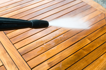 cleaning garden acacia table with a power washer - high water pressure cleaner on wooden exotic table surface  - focus on the tip of the spray nozzleの写真素材