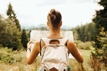 Hiking young woman traveler with backpack checks map to find directions in wilderness area, real explorer. Travel Conceptの写真素材