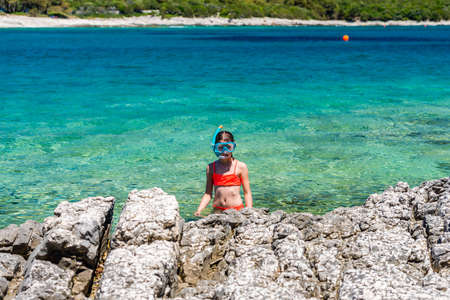 Little girl in a snorkeling mask coming out of the sea onto the rocky shoreの写真素材