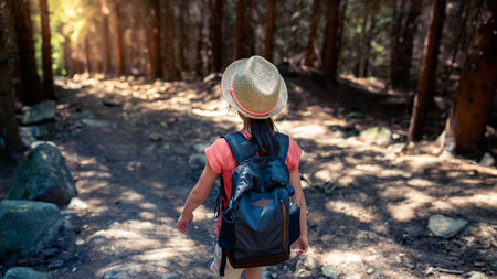 A young girl with a backpack is hiking in the forest. Back view.の写真素材