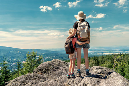 Young children with backpacks standing on top of a mountain and looking at the valleyの写真素材