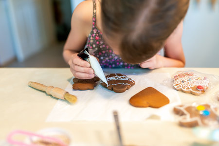Little girl decorating gingerbread cookies with glaze in the kitchenの写真素材