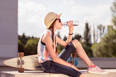 Beautiful young girl sitting on the roof and drinking water from a bottleの写真素材