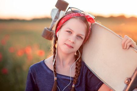 Portrait of a cute girl with skateboard in the poppy field at sunsetの写真素材
