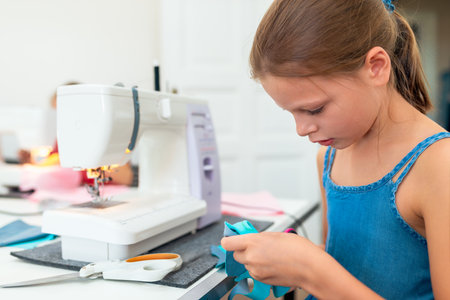 Little girl using a sewing machine to sew on a piece of fabric. Creative tailoring workshops for children - conceptの写真素材