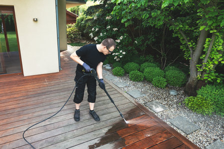 man cleaning terrace with a power washer - high water pressure cleaner on wooden terrace surfaceの写真素材