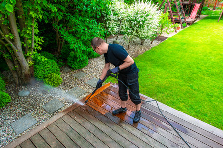 man cleaning terrace with a power washer - high water pressure cleaner on wooden terrace surfaceの写真素材