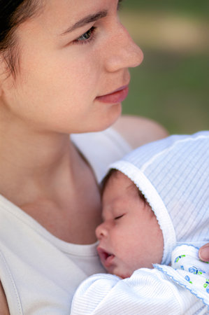 Newborn baby sleeping peacefully cradled in his mother's arms outdoorsの写真素材