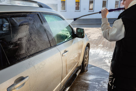Woman Using High-Pressure Washer to Clean a Dirty SUV at a Self-Service Car Washの写真素材