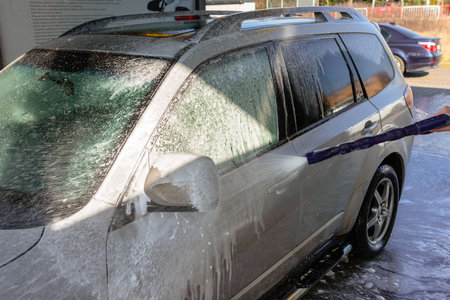 Washing an SUV with high-pressure water and foam at a self-service car wash, cleaning the vehicle exterior on a sunny dayの写真素材