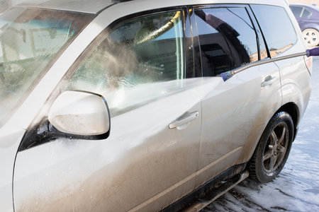 High-Pressure Water Spray Cleaning a Dirty Silver SUV at a Car Washの写真素材