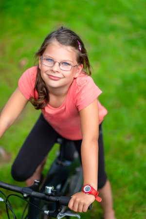 Young girl with glasses riding a bicycle outdoors in a green park, enjoying an active lifestyle and summer leisure timeの写真素材