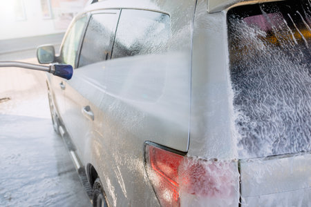 Washing an SUV with high-pressure water and foam at a self-service car wash, cleaning the vehicle exterior on a sunny dayの写真素材