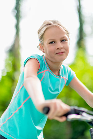 Smiling young girl riding a blue bicycle outdoors in a green park, enjoying an active lifestyle and outdoor fun in summerの写真素材