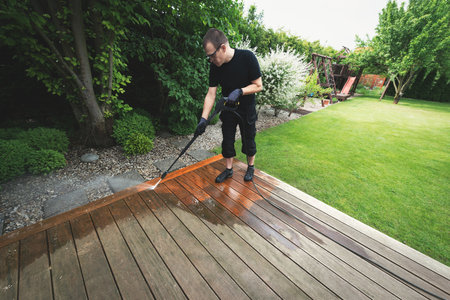 man cleaning terrace with a power washer - high water pressure cleaner on wooden terrace surfaceの写真素材