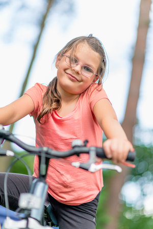 Young girl with glasses riding a bicycle outdoors in a green park, enjoying an active lifestyle and summer leisure timeの写真素材