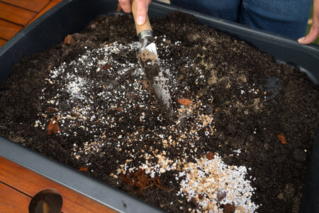 Hand mixing soil, perlite, coconut fiber and vermiculite with a garden trowel in a tray for planting, closeup of organic gardening preparation outdoorsの写真素材