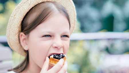 Closeup of girl in straw hat biting blueberry waffle with whipped cream at outdoor cafe, sweet summer dessert and foodie lifestyle momentの写真素材