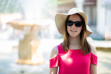 Woman in wide-brim hat and pink dress enjoying summer sunlight outdoors near city fountain, travel and fashion portrait, urban lifestyleの写真素材