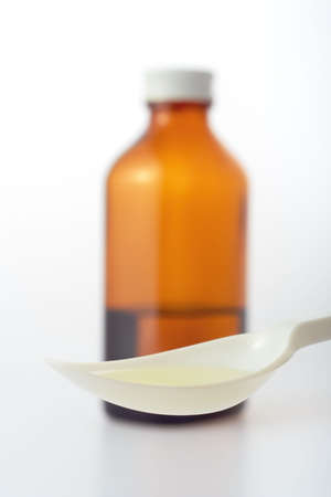 The close up of plastic spoon with yellowish drug on background of blunt brown bottle.の写真素材