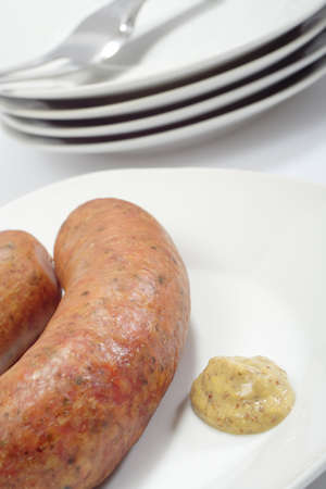 The close up view of sausage with portion of mustard and the heap of plates in background. Sharpness on mustard. Oblique view.の写真素材