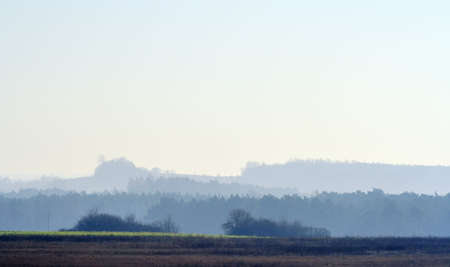 Hazy landscape with dark field strip on first plane and low hills covered by light hazeの写真素材