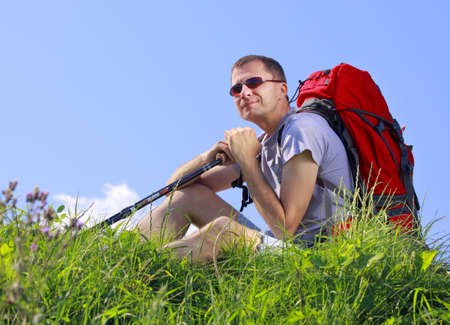 Man hiker with trekking sticks and backpack sit on a grassy meadowの写真素材