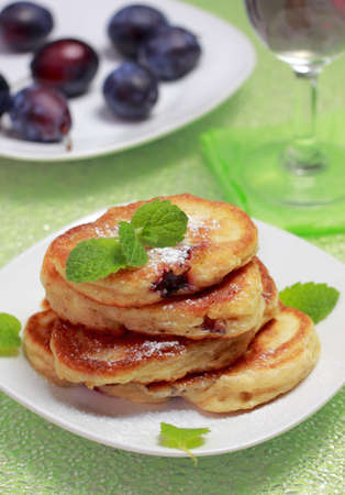 Stack of blinis (from white flour, with plum) topped with powdered sugar and mint on unfocused backgroundの写真素材