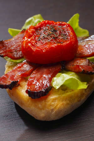 Half a bread roll with fried bacon, halved tomato and lettuceの写真素材