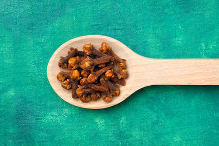 Cloves (Syzygium aromaticum) dried flower buds on wooden spoon over emerald painted textile backgroundの写真素材