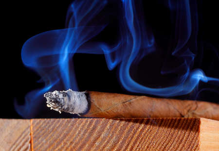 Cigar with abstract smoke. Wooden board, black background.の写真素材