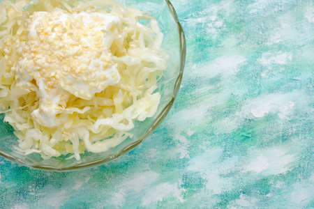 White cabbage salad with cream and sesame topping in bowl over painted textile background. Overhead view with copy space.の写真素材
