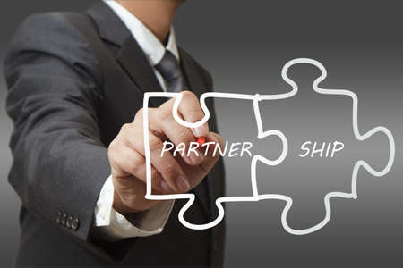 businessman drawing "partnership" written puzzle pieces on the transparent boardの写真素材