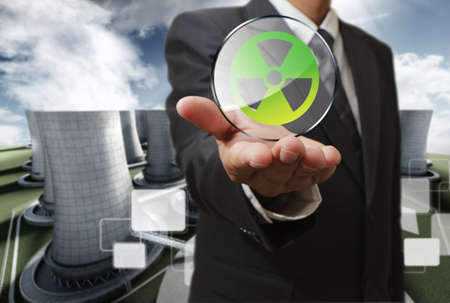 business man hand shows nuclear sign and nuclear power plant backgroundの写真素材