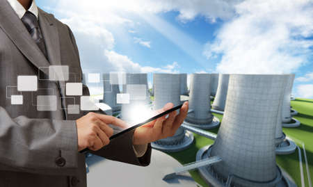 business man hand tablet computer and nuclear power plant backgroundの写真素材