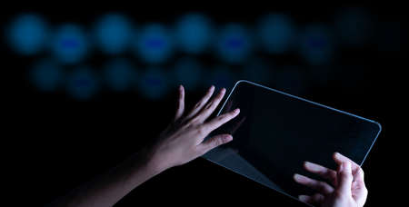 Woman hand holding and touch screen smart phone, tablet or cellphone on abstract blurred bokeh dark blue background background.の写真素材