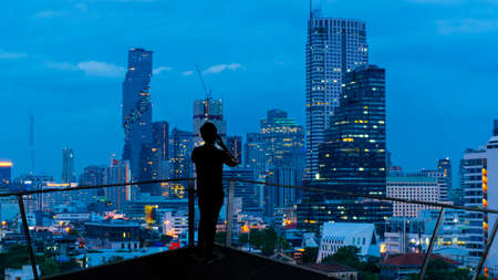 Businessman standing using smart phone on open roof top balcony watching city night view.Business...