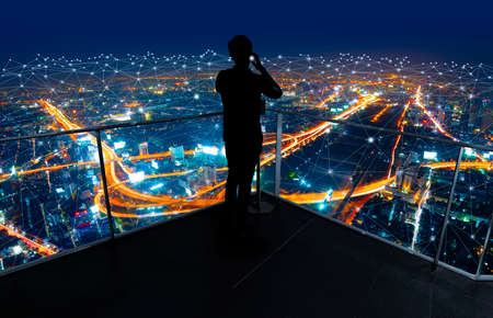 Businessman standing using smart phone in modern space watching city night view.Business Wireless network and Connection technology concept.の写真素材