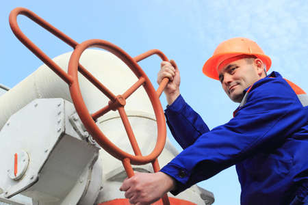 Worker turns big gas valve against sky, bottom view, close-upの写真素材