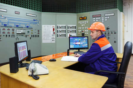 Engineer sitting writes in log on main control panel of gas compressor stationの写真素材